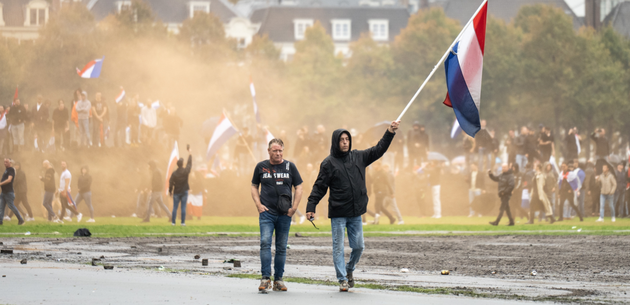 Mannen zwaaien met de Nederlandse vlag tijdens rellen op het Malieveld. 