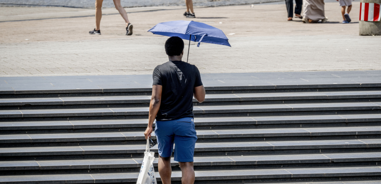 Een man loopt met een paraplu als bescherming tegen de zon