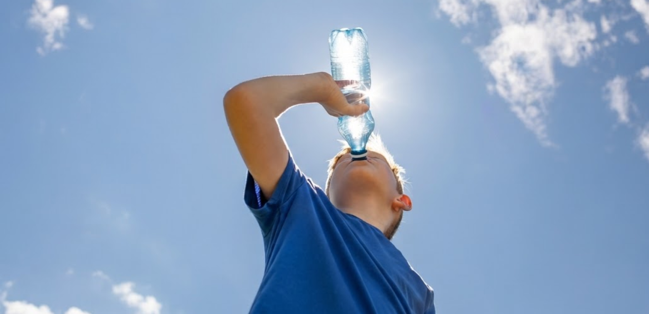 Kind drinkt water uit een flesje op een zonnige dag