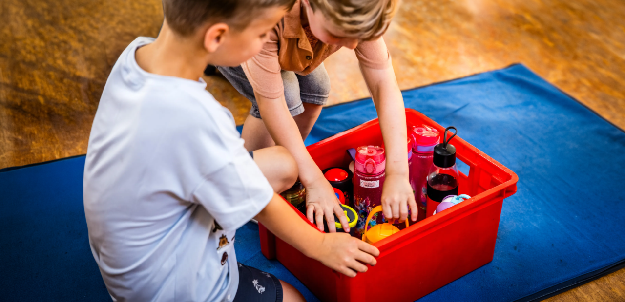 Twee kinderen pakken een bidon water uit een krat met bidons