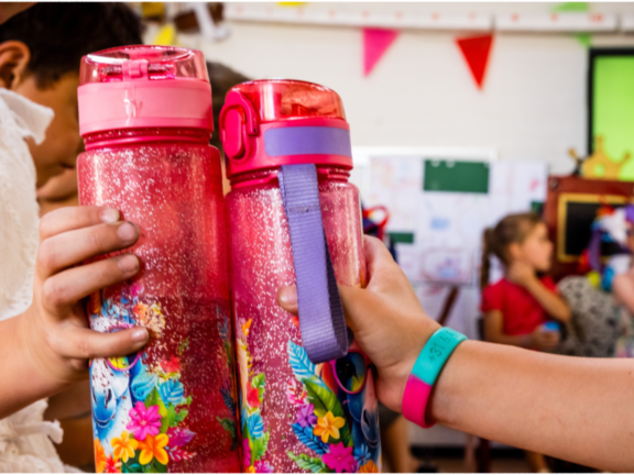 Twee kinderen in een klaslokaal die een waterflesje vasthouden. Op de achtergrond nog drie kinderen.