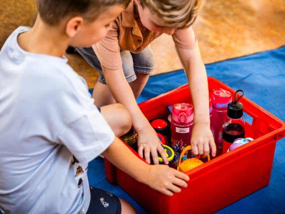 Twee kinderen pakken een bidon water uit een krat met bidons