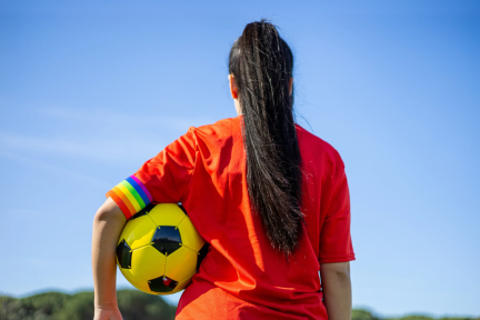 Foto van de achterkant van een persoon met een voetbal onder diens arm en een regenboogband onderaan de mouw