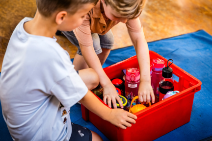 Twee kinderen pakken een bidon water uit een krat met bidons
