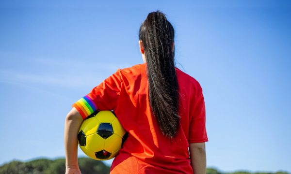 Foto van de achterkant van een persoon met een voetbal onder diens arm en een regenboogband onderaan de mouw