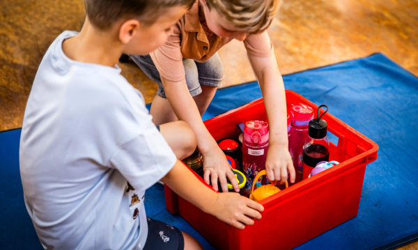 Twee kinderen pakken een bidon water uit een krat met bidons